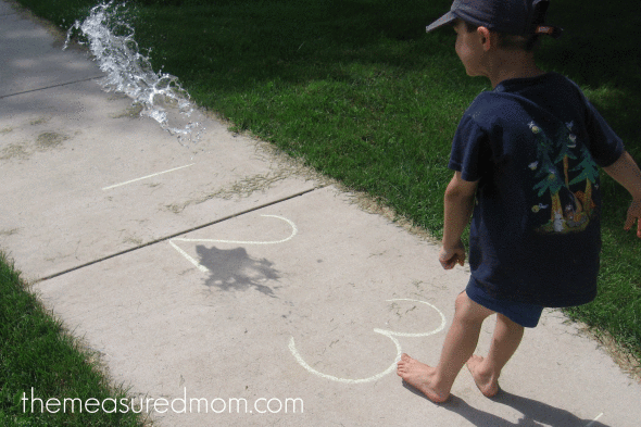 child doing water balloon math (throwing water balloon on correct chalk number)