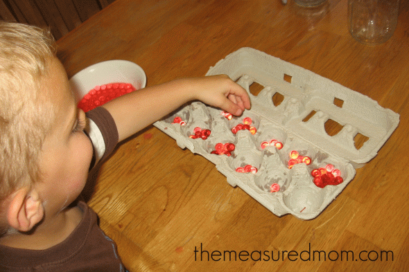 child doing math activity (placing water beads in an egg carton)