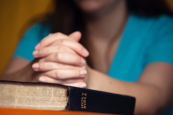 Girl praying with hands on 150 year old Bible